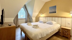 A bedroom with a bed, a TV, a window, and a painting on the wall.