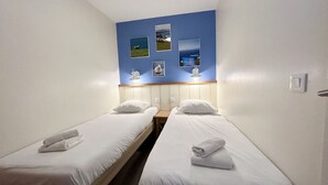 Ett hotellrum med två separata sängar, ett träbord vid sängen och en blå vägg med inramade tavlor.