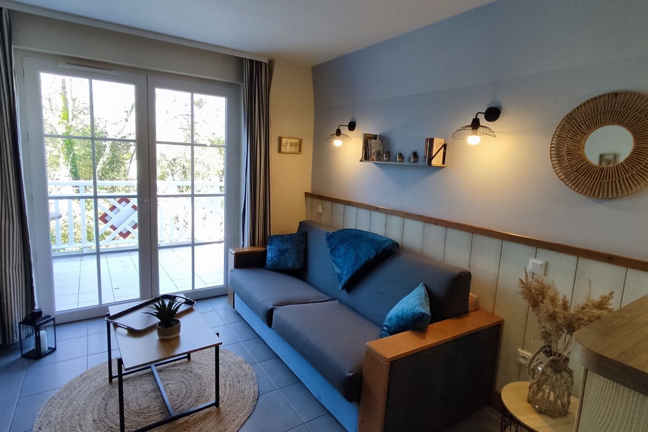 A living room with a sofa, a coffee table, and a large window with curtains.