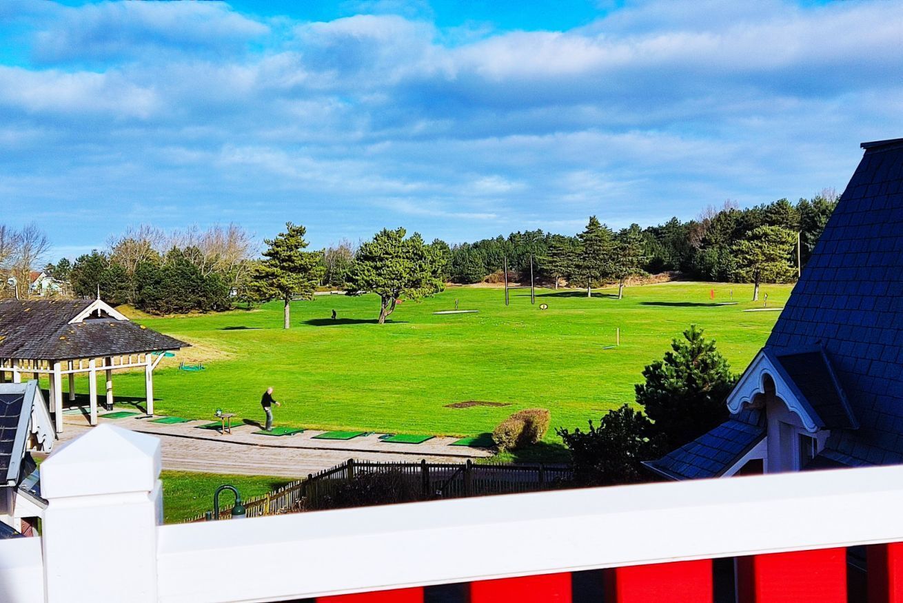 A golf course with a pavilion, surrounded by trees and residential buildings.