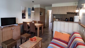 A compact living space with a TV, dining area, kitchenette, and a sofa. - Appartement Belle Dune 1 Chambre (Fort-Mahon Plage)