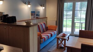 A cozy living area with a sofa, a dining table, and a kitchen area with appliances. - Appartement Belle Dune 1 Chambre (Fort-Mahon Plage)
