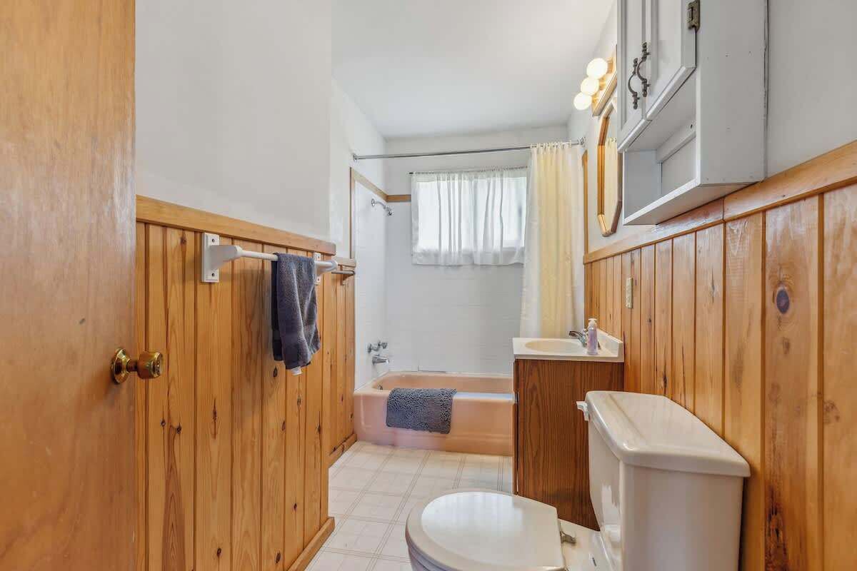 Een badkamer met houten lambrisering, een toilet, een bad en een wastafel.
