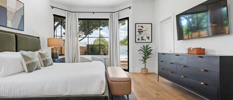 Een slaapkamer met een groot bed, een kaptafel, een televisie en een raam met gordijnen.