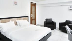 A modern hotel room with a large bed, two black leather chairs, a wooden door, and a wall-mounted air conditioning unit. - SOFT HOTEL (Douala)