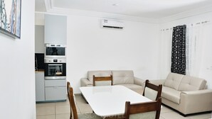 A modern living room with a sofa, a dining table, and a kitchen area with an oven and microwave. - SOFT HOTEL (Douala)