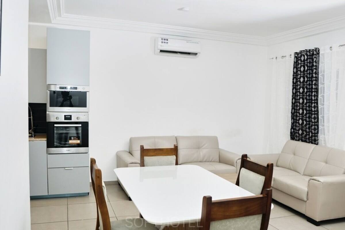 A modern living room with a sofa, a dining table, and a kitchen area with an oven and microwave.