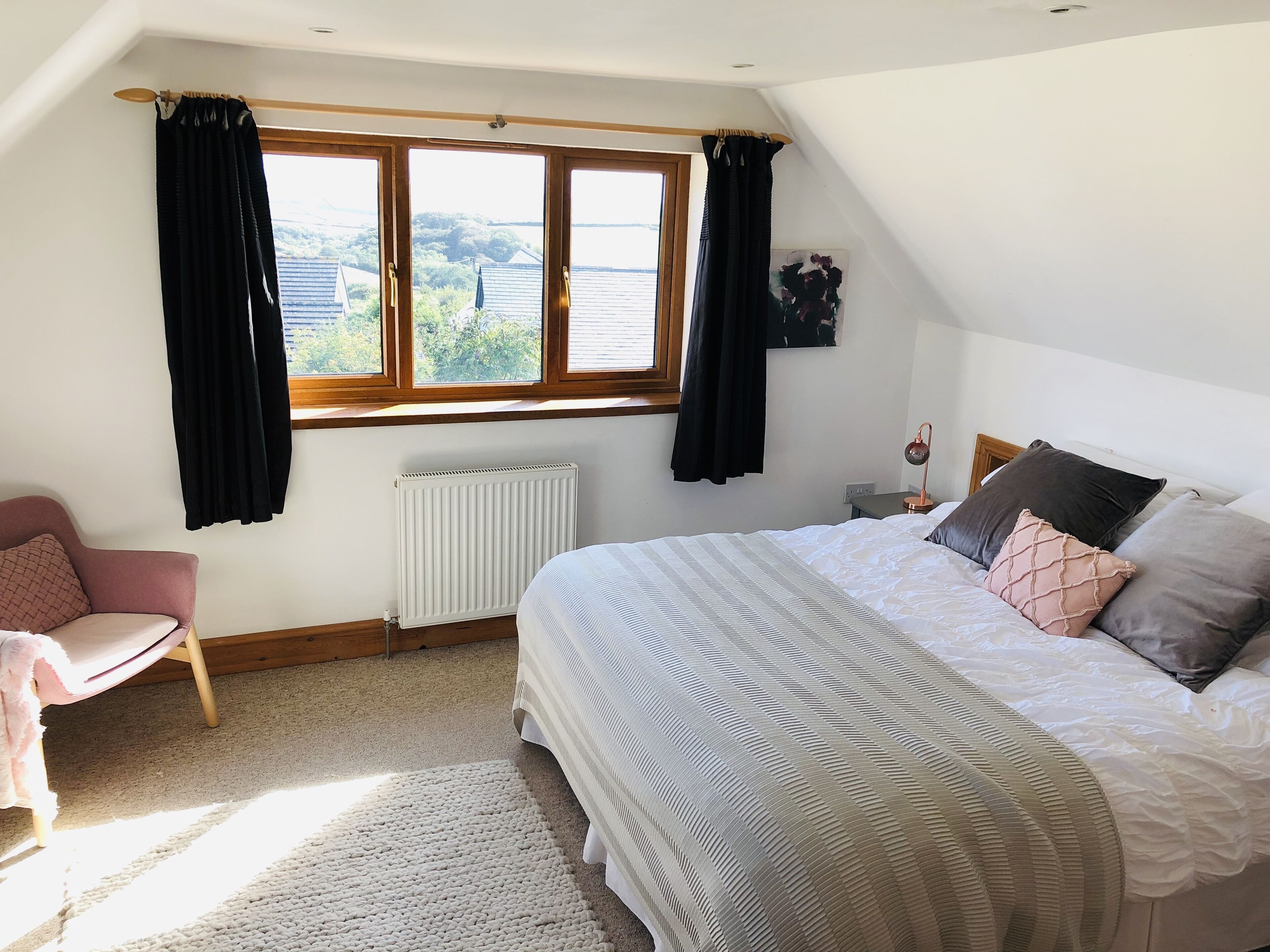 A bedroom with a large bed, a chair, a radiator, and a window with curtains.