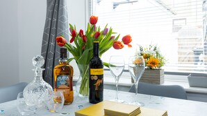 Uma mesa com uma garrafa de whisky, um vaso de tulipas, duas taças de vinho e uma pilha de cadernos amarelos.