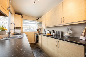 Eine moderne Küche mit Holzschränken, einer Edelstahlspüle und einem Fenster mit Jalousien.