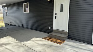 A house with a dark exterior, a white front door, a small window, and a welcome mat. - Miller Beach Family Getaway (Gary)