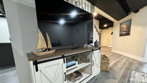 A modern living room with a wooden entertainment unit, a sailboat model, and a flat-screen TV. - Miller Beach Family Getaway (Gary)