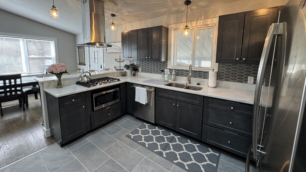 A modern kitchen with dark cabinets, a stainless steel refrigerator, a gas stove, and pendant lighting. - Miller Beach Family Getaway (Gary)