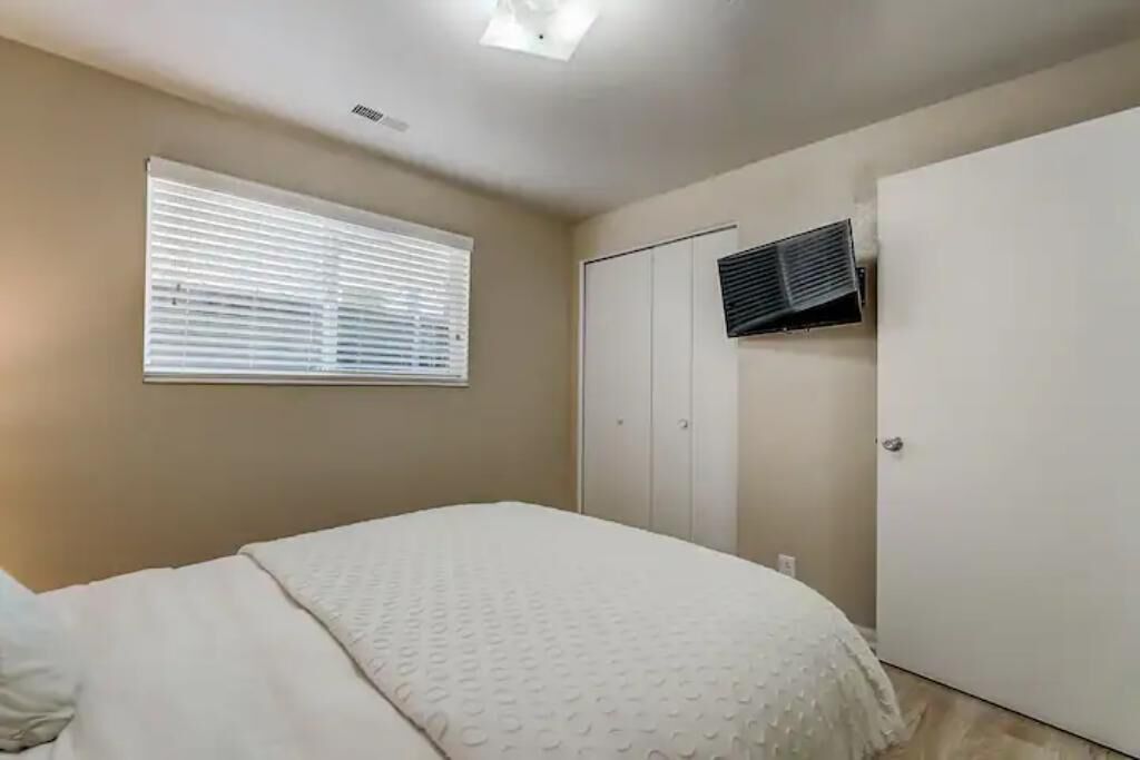 A bedroom with a bed, a window with blinds, a wardrobe, and an air conditioning unit.