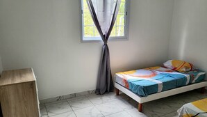 Una habitación pequeña y limpia con una cama, un armario de madera y una ventana con cortinas.