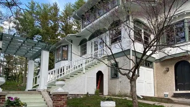 Une maison à deux étages avec un porche à l’avant, un escalier et des fondations en briques.