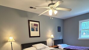 A bedroom with a large bed, two bedside tables with lamps, a ceiling fan, and a window with a view of trees. - Unplug and unwind at your Leonardtown waterfront vacation home! (Leonardtown)