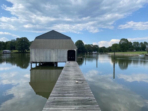 A concrete covered structure with a wooden dock extending into calm water, surrounded by trees and a clear sky. - Unplug and unwind at your Leonardtown waterfront vacation home! (Leonardtown)