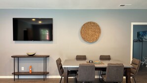 A dining area with a table and chairs, a flat-screen TV mounted on the wall, and a woven wall decoration. - Unplug and unwind at your Leonardtown waterfront vacation home! (Leonardtown)