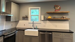 A modern kitchen with grey cabinets, a stainless steel range hood, a built-in oven, a dishwasher, and a window with a view of greenery. - Unplug and unwind at your Leonardtown waterfront vacation home! (Leonardtown)
