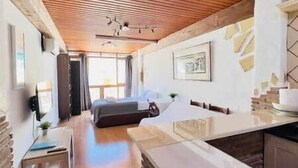 Een moderne kamer met een bed, een klein tafeltje, een kitchenette en een groot raam.