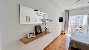 Habitación de hotel con un espejo grande, repisa con cuadros enmarcados, planta en maceta y una cama.