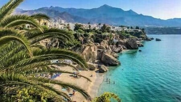 Un pueblo costero con playa, acantilados rocosos y montañas al fondo.