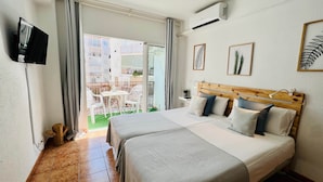 Habitación de hotel con cama, televisión, balcón con mesa y sillas, y vista a edificios.