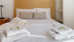 A neatly made bed with white linens, two pillows with a geometric pattern, and a folded towel with a green bottle on it. - Apartment Chanquete in the center of Nerja - South Costa (Nerja)