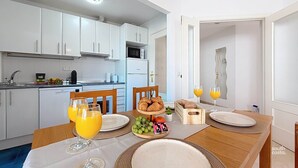 A modern kitchen with white cabinets, a microwave, and a dishwasher. There is a dining table set with plates, glasses, and a fruit basket. - Apartment Chanquete in the center of Nerja - South Costa (Nerja)