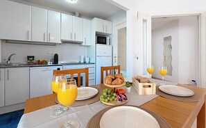Een moderne keuken met witte kasten, een magnetron en een vaatwasser. Er staat een eettafel gedekt met borden, glazen en een mand met fruit.