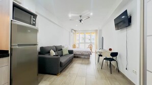 A compact living space with a kitchenette, a sofa, a dining table with chairs, and a TV mounted on the wall.