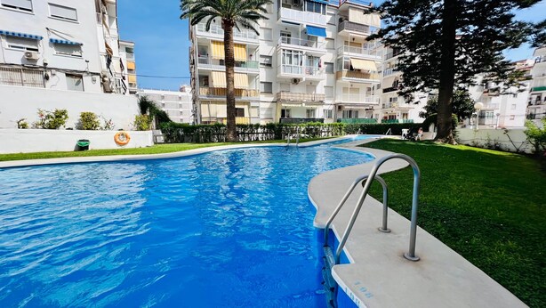 A swimming pool with a metal ladder, surrounded by a well-maintained lawn and a multi-story residential building in the background.
