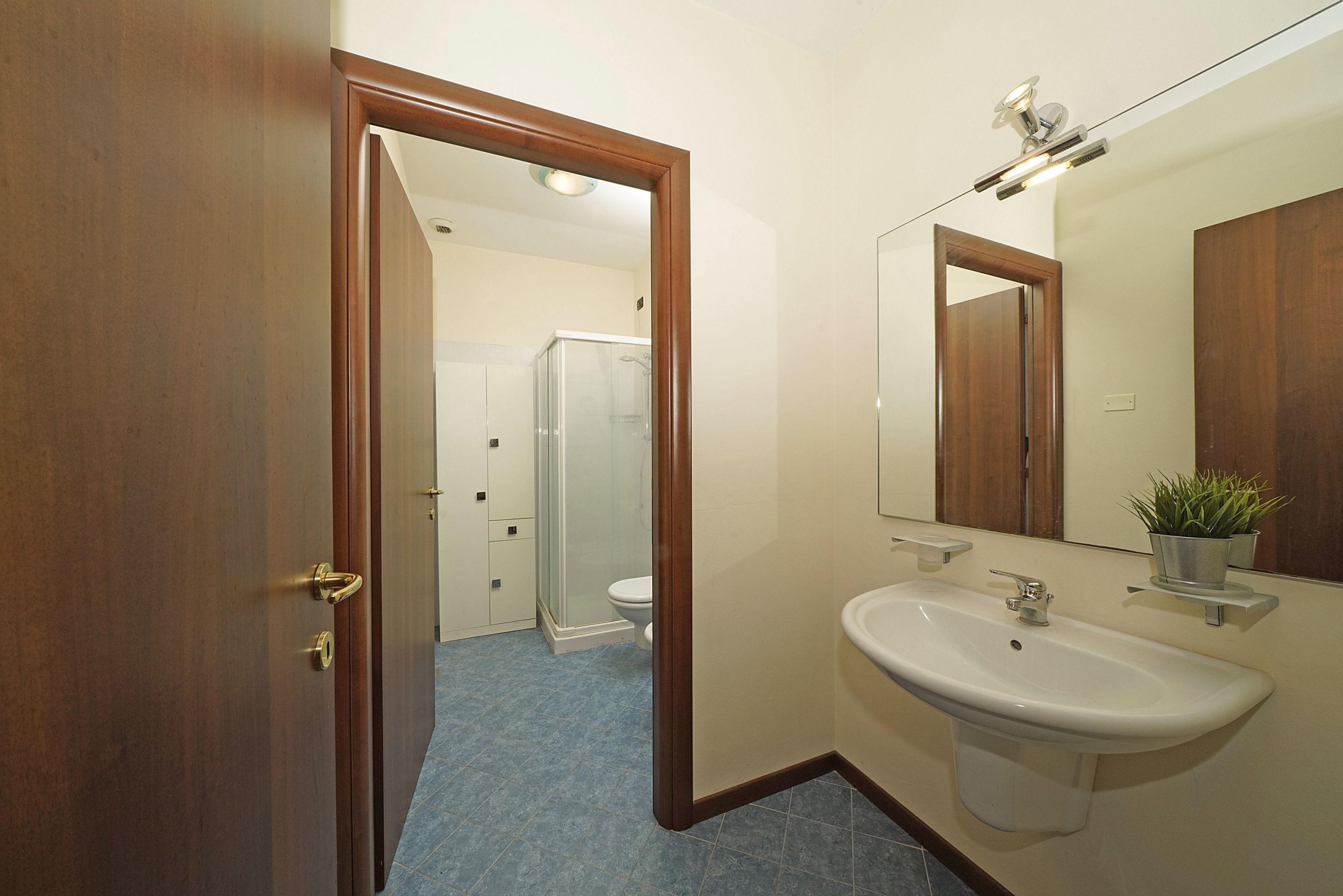 Un baño con puerta de madera, un lavabo blanco, un espejo y una zona de ducha.