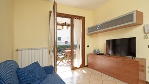 Ein Wohnzimmer mit einer Couch, einem Fernseher, einer Holzeinrichtung und einer Glastür zum Außenbereich.