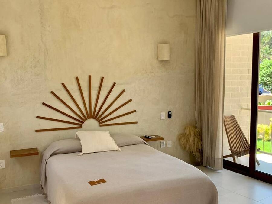A bedroom with a large bed, a ceiling fan, a sunburst headboard, a bedside table, and a view of the outdoors through a sliding glass door.