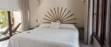 Un dormitorio con cama, ventilador de techo, ventana grande con cortinas y vista a palmeras.