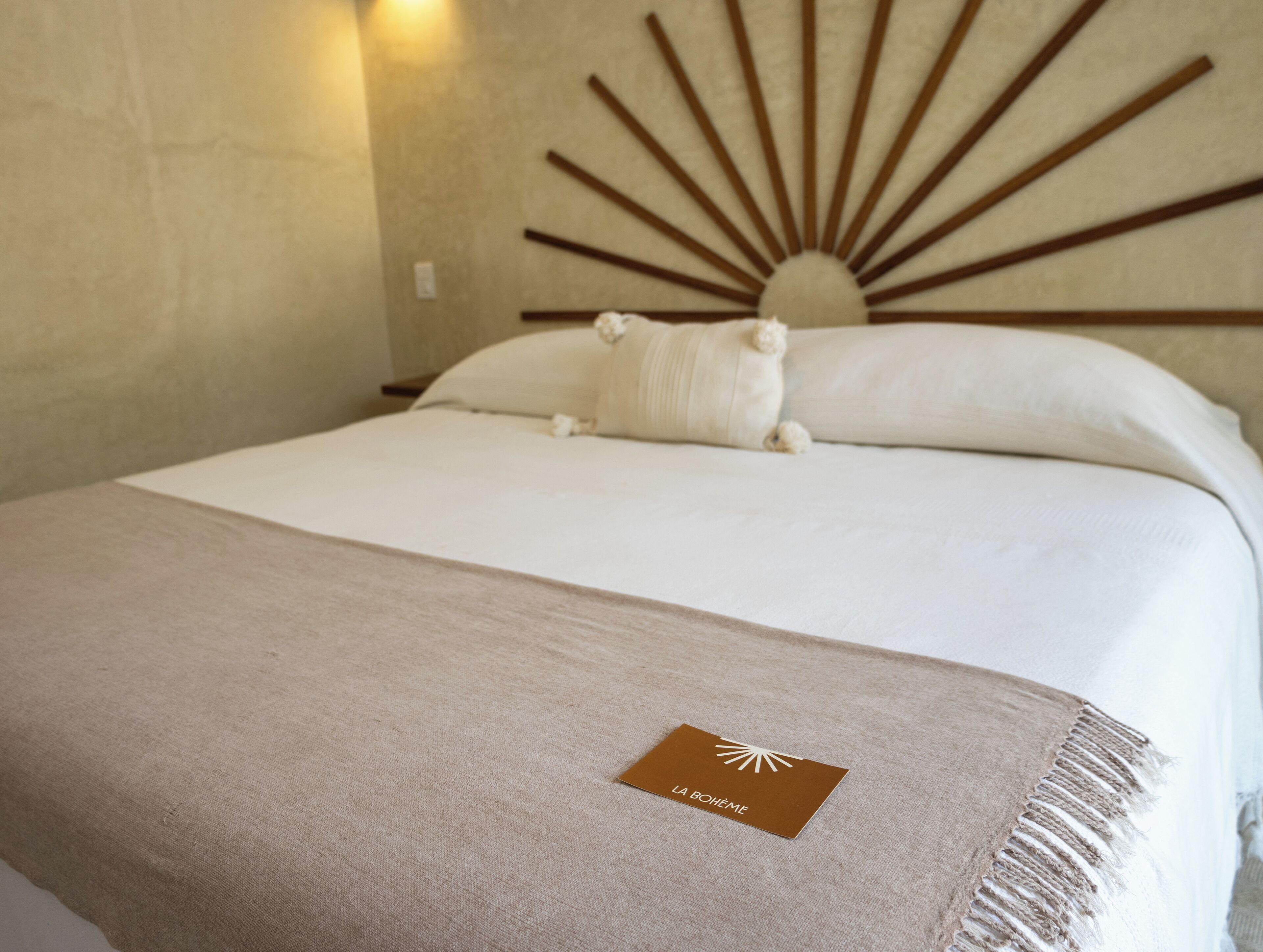 Een net opgemaakt bed met een beige deken en een kussen met een logo.