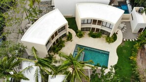 Een modern resort met een centraal gelegen zwembad, omringd door palmbomen en witte gebouwen.
