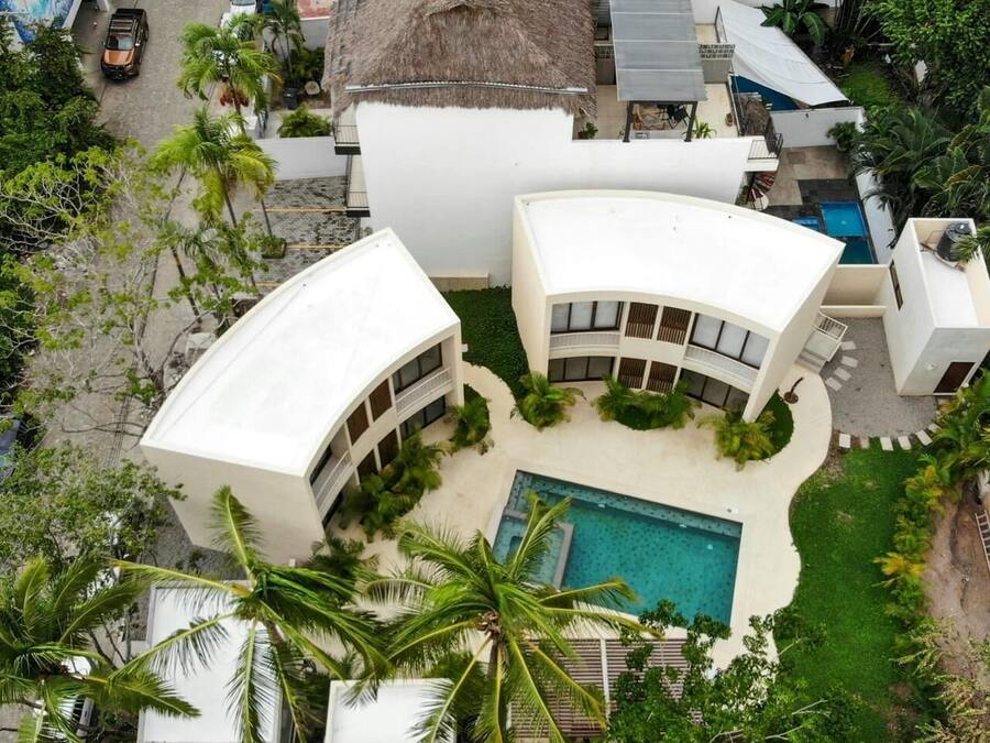 Ein modernes Resort mit einem zentral gelegenen Pool, umgeben von Palmen und weißen Gebäuden.