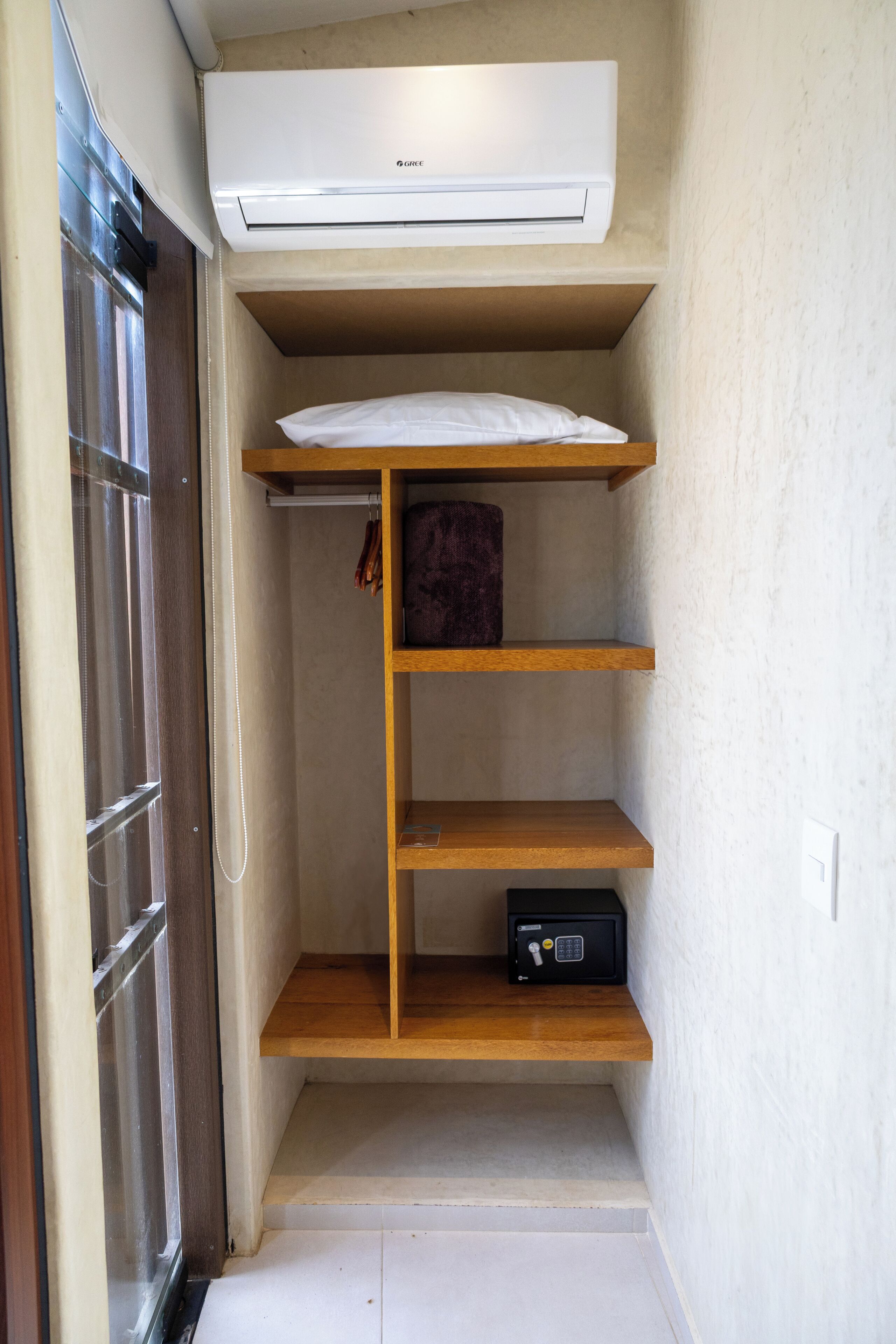 A compact storage space with a white air conditioner, wooden shelves, and a small safe.