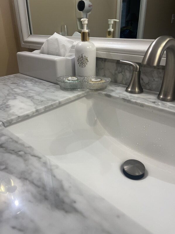 A bathroom sink with a marble countertop, a white soap dispenser, and a glass soap dish. - Cozy newly renovated condo, in Norwich, CT. 3 mins from Mohegan Sun Casino. (Norwich)