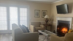 A living room with a fireplace, a sofa, a coffee table, and a television mounted on the wall. - Cozy newly renovated condo, in Norwich, CT. 3 mins from Mohegan Sun Casino. (Norwich)