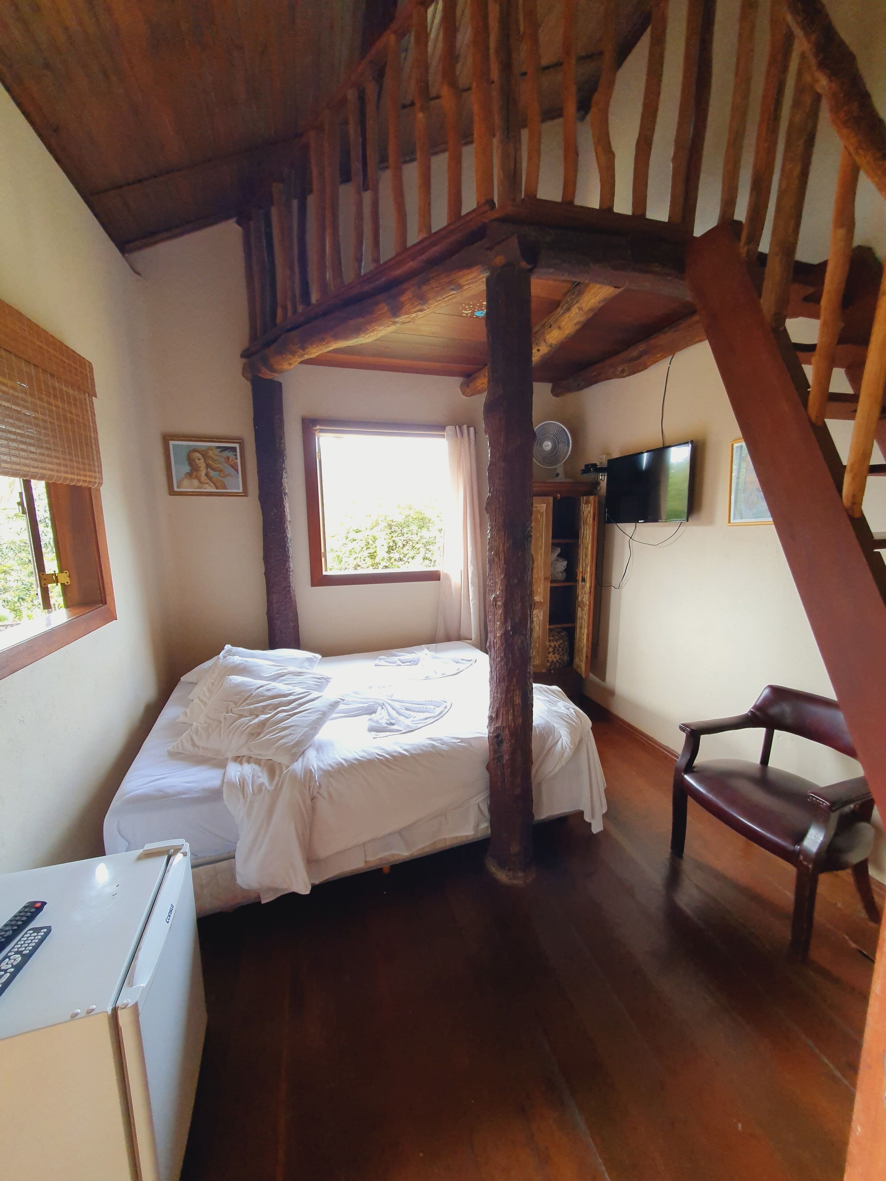 Un dormitorio con una cama, una silla, un televisor y una ventana.
