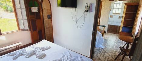 A bedroom with a bed, a television mounted on the wall, and a view of the kitchen through an open doorway.