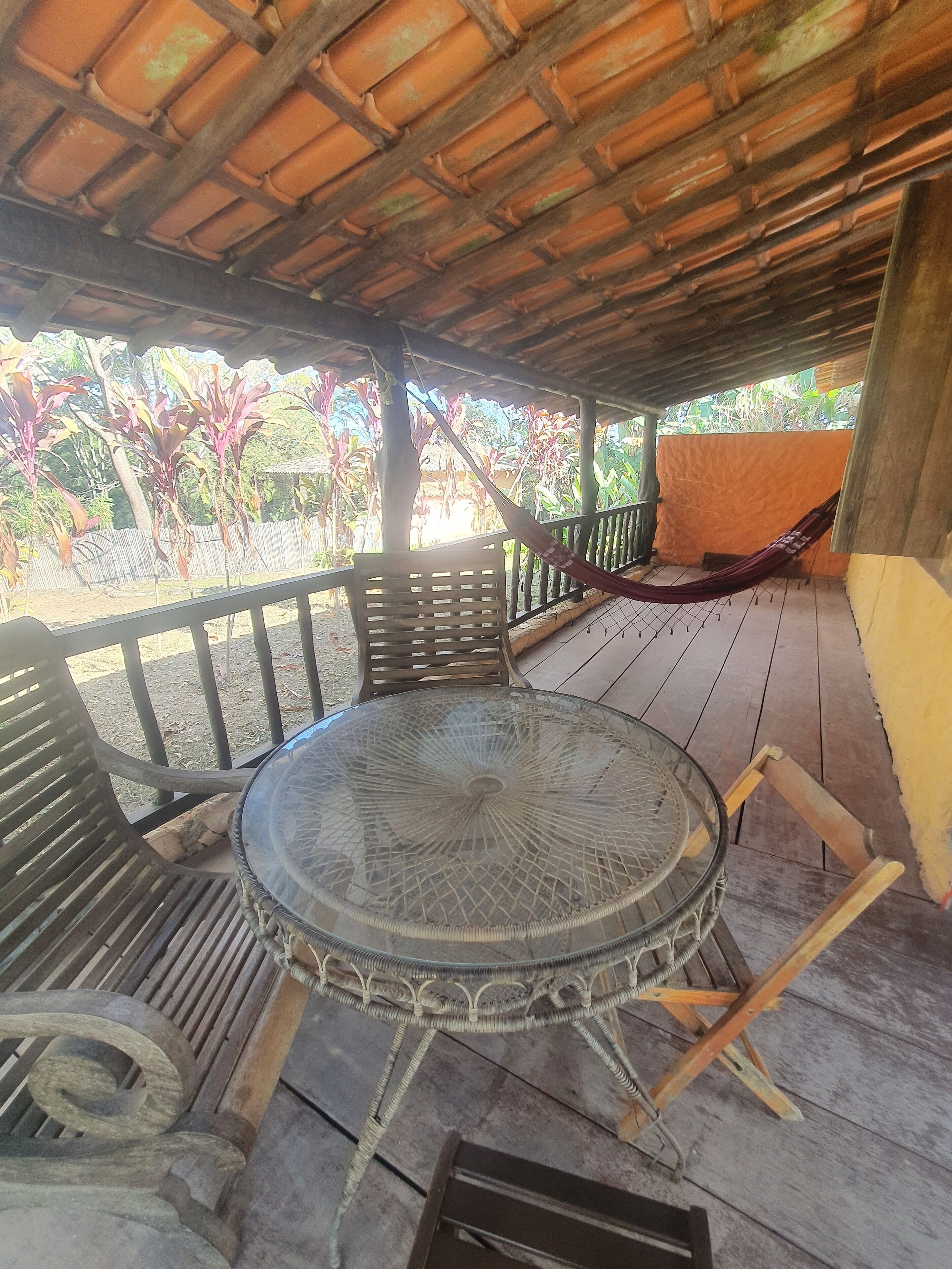 A covered outdoor seating area with a round glass table, wooden chairs, and a hammock.