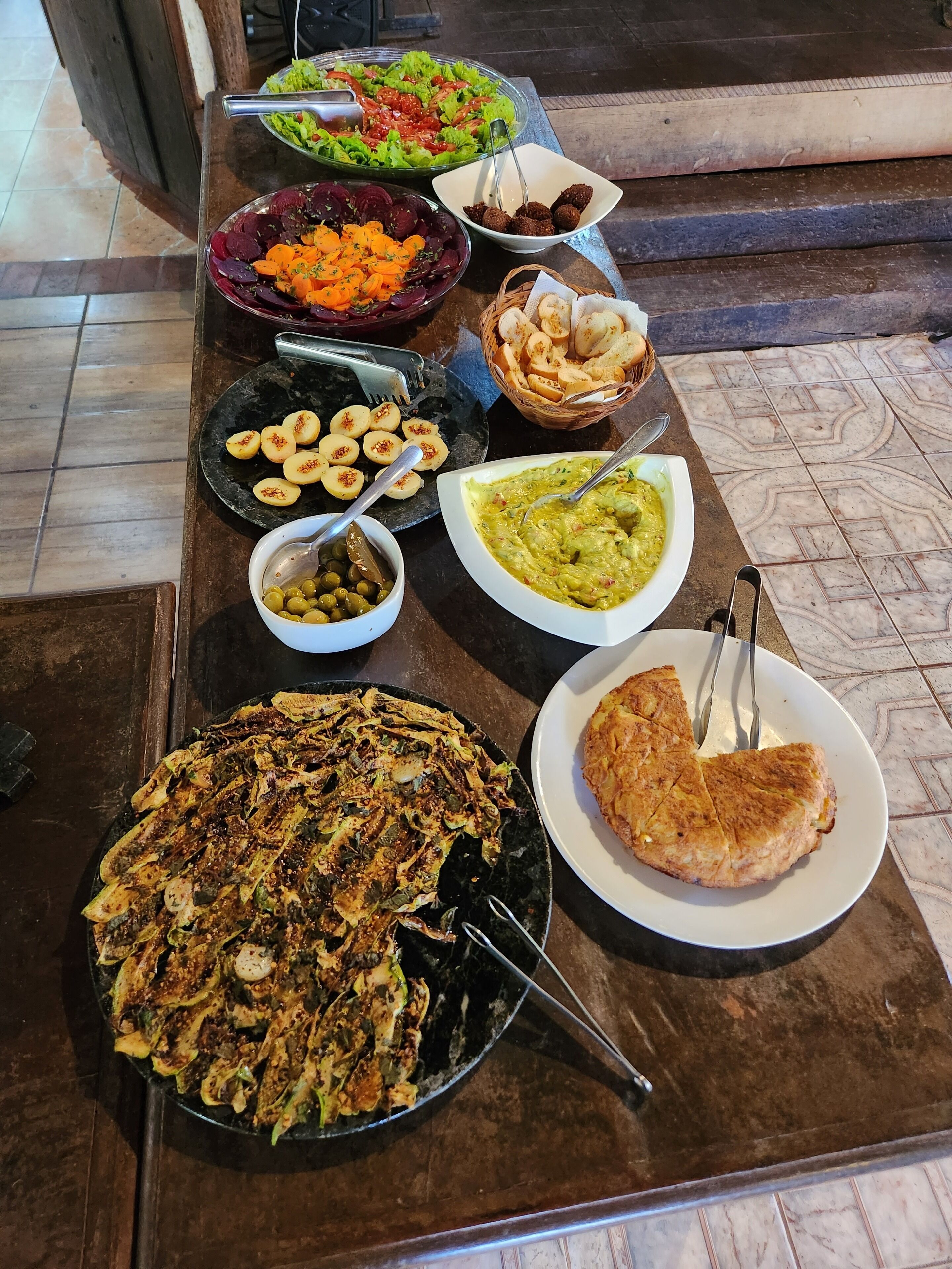 A buffet table with various dishes including a salad, beets, falafel, and a large platter of fried food.