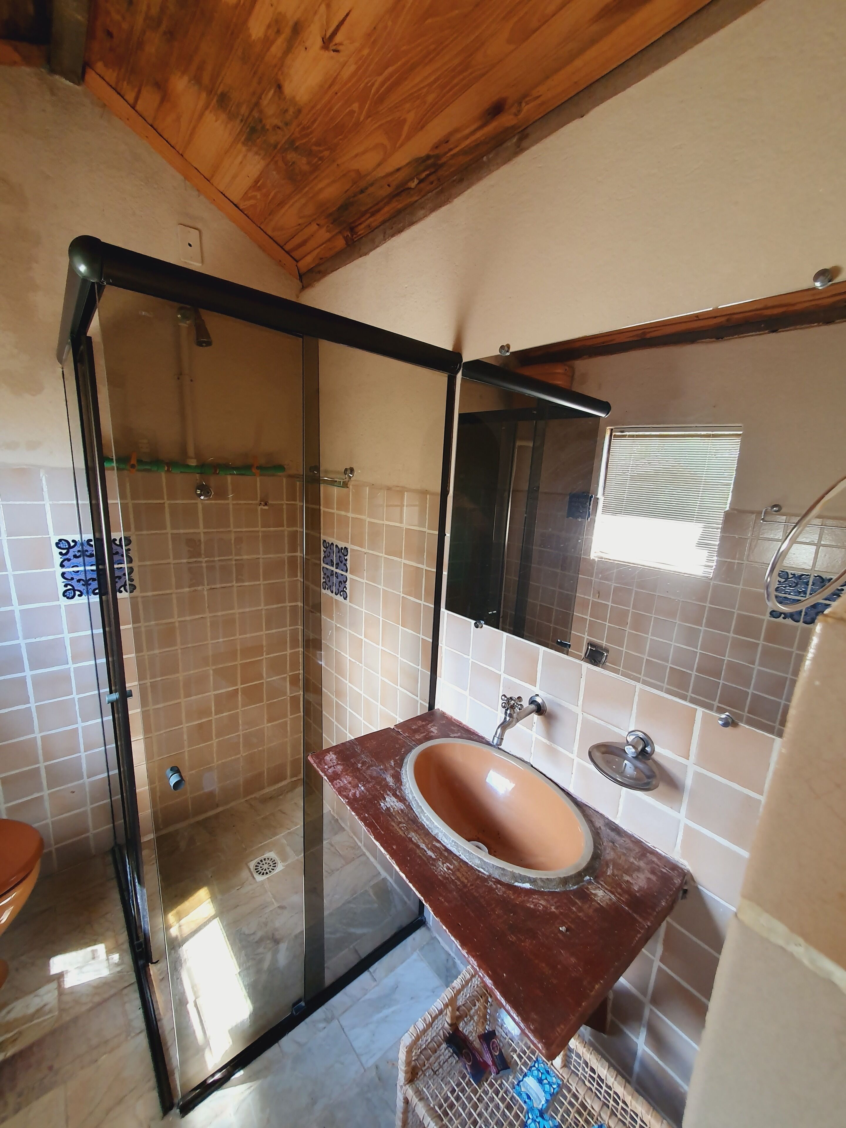 Un baño con ducha envuelta en vidrio, techo de madera, paredes con azulejos y lavamanos de mármol.