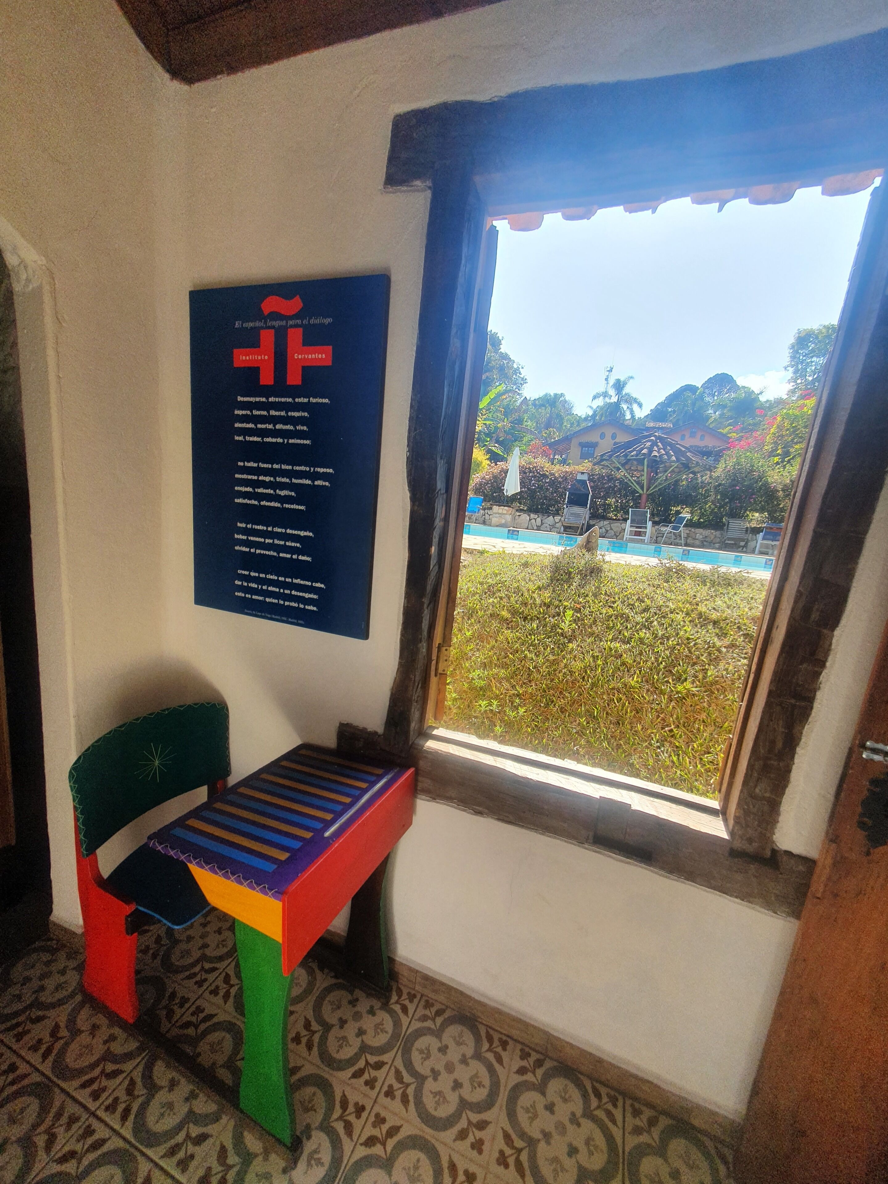 A room with a window, a chair, a table, and a poster on the wall.