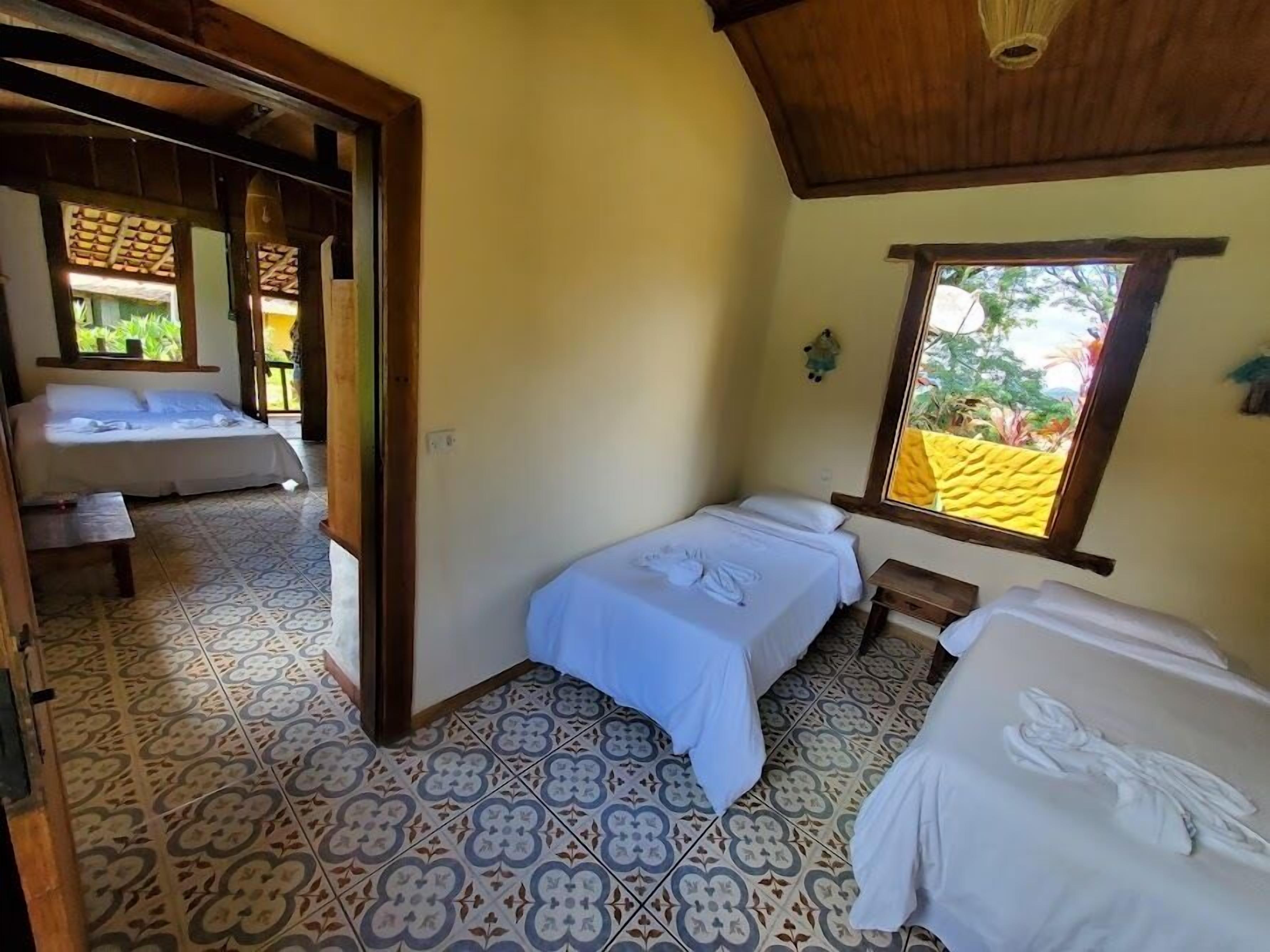 A room with two beds, a window with a yellow view, and patterned floor tiles.
